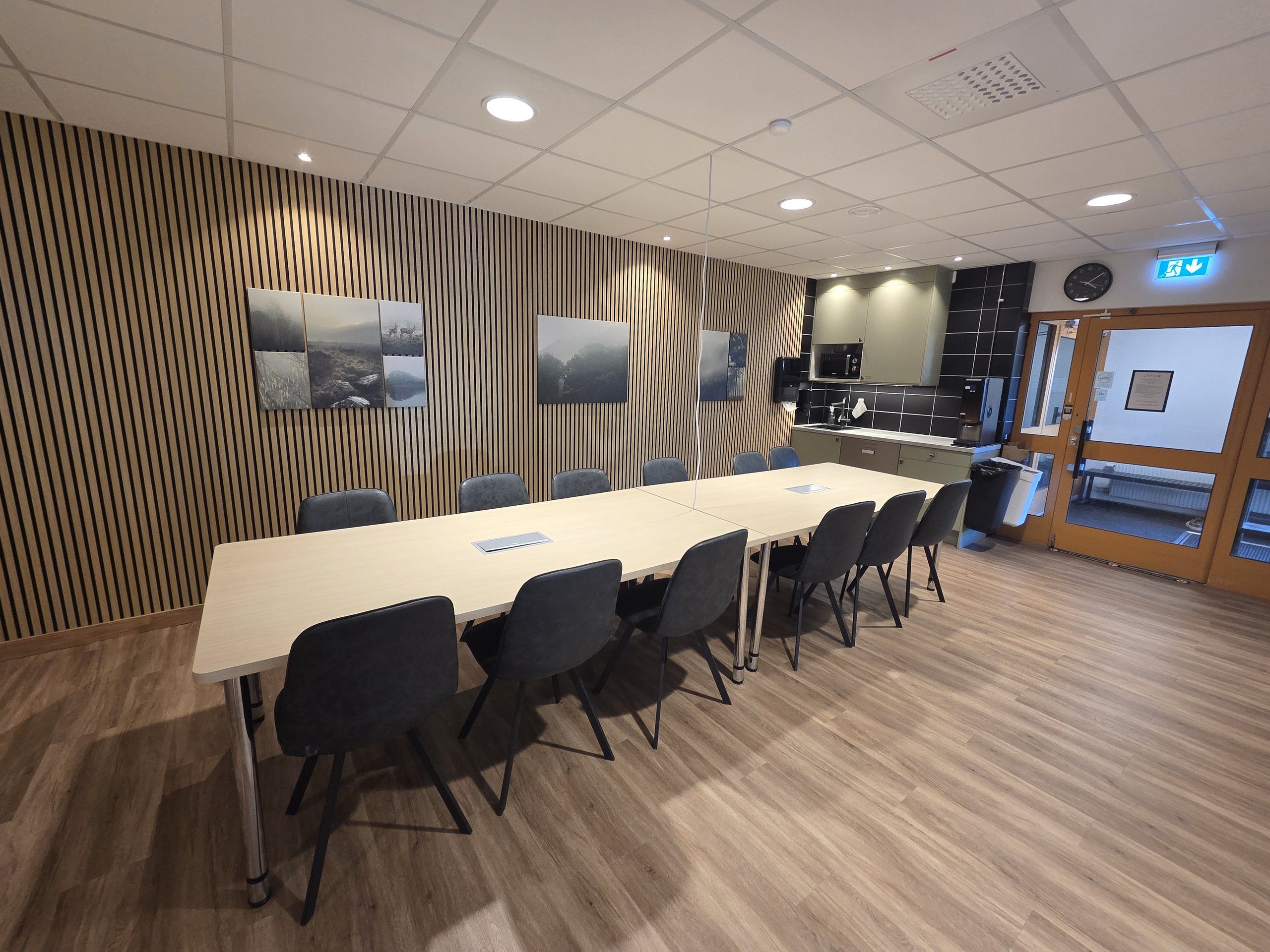 Loungen med långt bord, grå stolar, pentry och mikrovågsugn